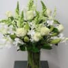 Tall arrangement of white roses, lilies, orchids, and snapdragons in a clear glass vase