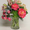 Pink peonies, tulips, lilies, and green hydrangea arranged in a clear glass vase