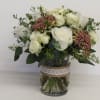 White roses and pink filler flowers in a glass vase with lace ribbon