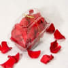Clear gift box filled with red rose petals and tied with a gold ribbon