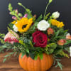 Floral arrangement in a pumpkin container with roses, sunflowers, and mixed blooms