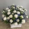White carnations and blue flowers arranged in a white basket