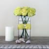 Yellow roses in a clear rectangular vase with a yellow ribbon and candle beside it