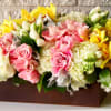 Pink roses and yellow orchids arranged in a rectangular box with white blooms