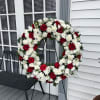 Red roses and white chrysanthemums arranged in a large wreath on a stand