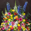 Large colorful funeral spray with lilies, roses, gerberas, and blue delphinium