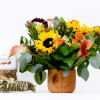 Bouquet of sunflowers, orange roses, and calla lilies in a terracotta vase