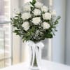 White roses arranged in a clear vase with a white ribbon.