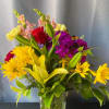 Mixed bouquet of yellow daisies, lilies, and purple flowers in a clear vase