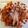 Orange autumn wreath with plaid ribbon on a white door