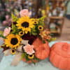 Sunflower bouquet with pink carnations and ribbon beside decorative pumpkins