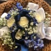 White roses and blue flowers arranged with ribbon on a brown textured background