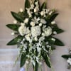 White funeral spray with roses, lilies, and orchids on an easel
