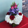 Bouquet of red roses, white hydrangeas, purple daisies, and pink tulips in a glass vase
