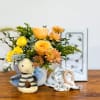 Baby-themed gift set with yellow and peach flowers in a vase, bee plush toy, and bee-print blanket.