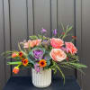 Mixed bouquet in a white ribbed vase with pink, peach, and purple blooms