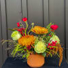 Bright mixed flower arrangement in a terracotta pot with orange and green blooms