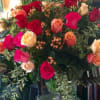 Large bouquet of red, pink, and peach roses with berries in a clear glass pedestal vase