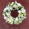 White floral wreath on a black stand with roses and lilies
