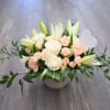 Low floral arrangement of white roses, lilies, and peach spray roses in a patterned vase