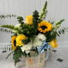 Yellow roses and sunflowers in a baby-themed container with a blue ribbon.