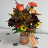 Mixed bouquet in a pumpkin spice candle jar with a striped ribbon