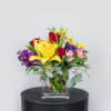 Mixed bouquet of yellow lilies, red roses, and purple flowers in a glass vase