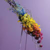 Tall multicolored floral arrangement on a stand against a purple background