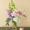 Pink lilies, roses, hydrangea, and purple stock in a glass vase