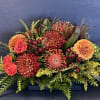 Low floral arrangement with orange and red blooms in a rectangular container