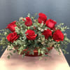 Red roses arranged in a low red container with eucalyptus foliage