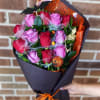 Bouquet of pink and red roses wrapped in black paper with orange ribbon