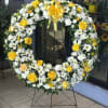 Bright yellow roses and crisp white daisies form a circular sympathy wreath