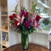 Tall bouquet of red roses and pink lilies in a green glass vase