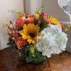 Mixed bouquet with sunflowers, coral roses, white hydrangea, and pink buds in a green vase