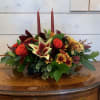 Low floral centerpiece with red candles and orange roses in a dark container