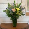 Mixed bouquet with roses, lilies, and blue flowers in a tall green vase