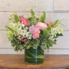 Pink and white mixed flower arrangement in a clear glass cylinder vase lined with green leaves