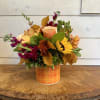 Autumn flower arrangement in an orange plaid container with yellow and peach blooms