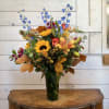 Mixed bouquet with sunflowers, lilies, and blue delphinium in a tall vase