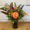 Peach roses in a dark glass vase with purple and yellow flowers