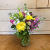 Mixed bouquet of yellow, pink, white, and purple flowers in a glass vase