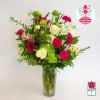 Mixed pink, white, and green flowers arranged in a tall glass vase