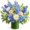 Blue and white floral arrangement with peach roses in a green glass vase