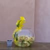 Yellow orchids arranged in a round glass bowl with a small square candle holder beside it