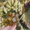 Amber glass watering can held in front of a moss wall
