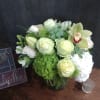 Green and white floral arrangement in a glass vase with orchids and roses