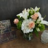 Bouquet of white lilies, peach roses, and white hydrangeas in a glass vase