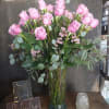 Pink roses arranged in a tall glass vase with eucalyptus and small filler flowers.