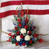 Red, white, and blue floral standing spray in front of a flag